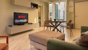 A modern living room with a flat-screen TV displaying Netflix, a dining area with a table and chairs, and a view of the outside through a glass door. - Modern loft, steps away from the Tower of Pisa (Pisa)