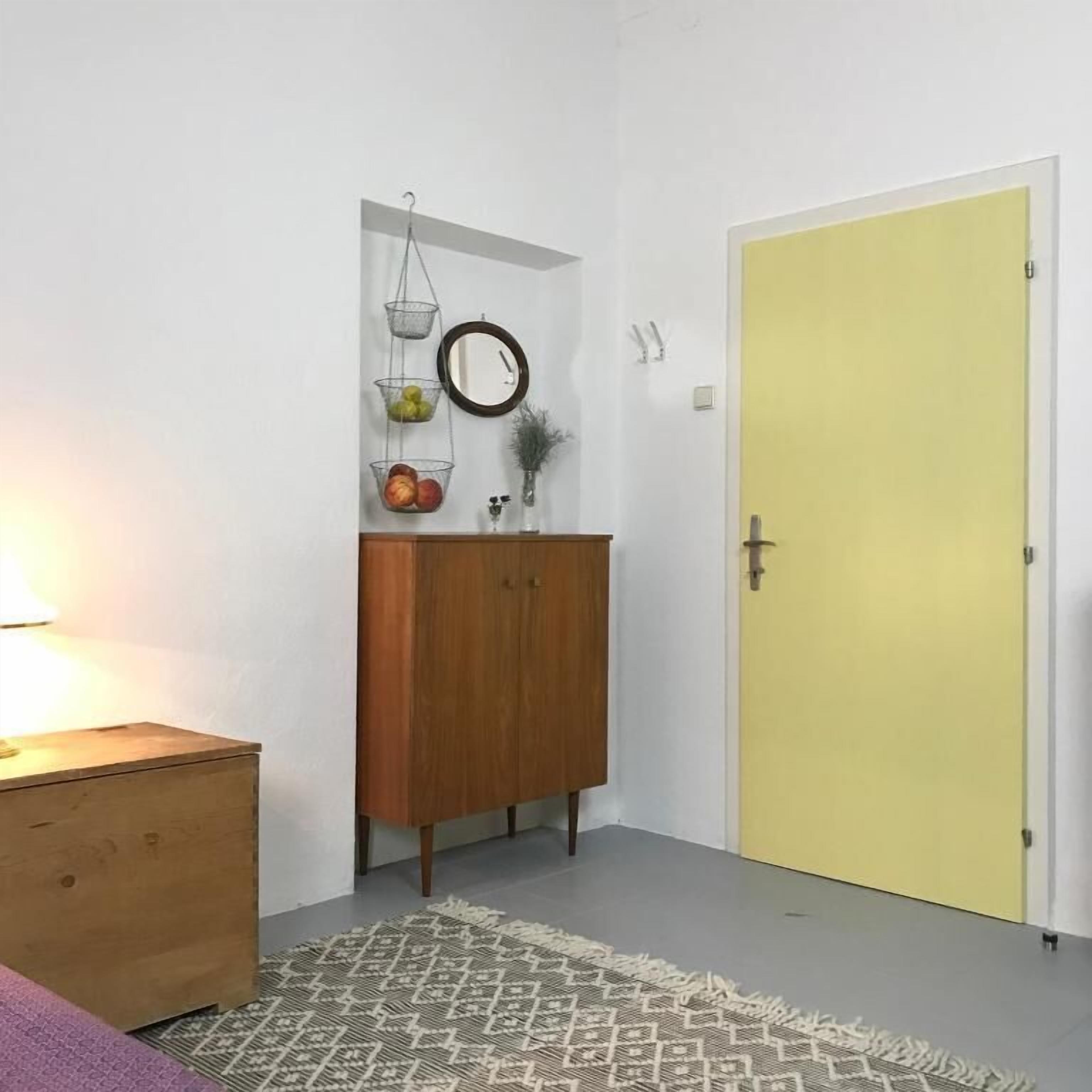 A room with a wooden cabinet, a yellow door, and a patterned rug.