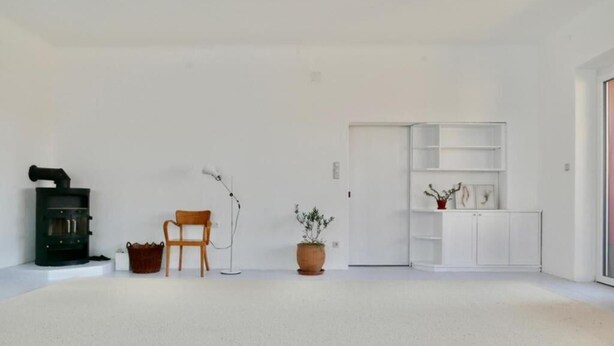 A minimalist living room with a fireplace, a chair, a floor lamp, and a white cabinet with shelves. - Unter einem Dach (Raabs An Der Thaya)