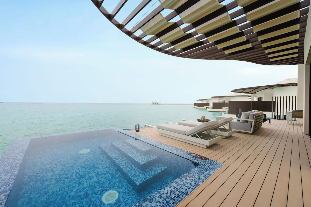 A luxurious outdoor swimming pool area with a wooden deck, lounge chairs, and a view of the sea.