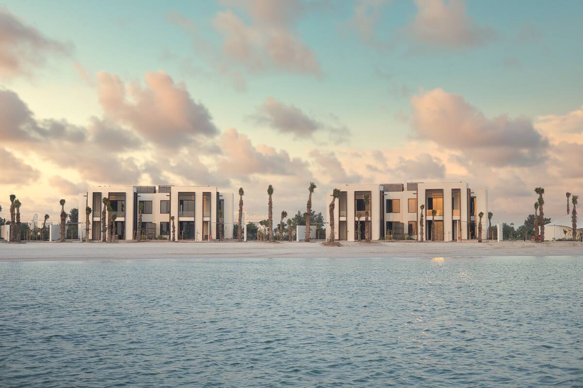 A beachfront hotel with modern architecture, a pool, and palm trees.