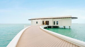 A modern overwater bungalow with a wooden deck leading to a private pool, surrounded by clear turquoise water. - Hawar Resort By Mantis (Hawar)