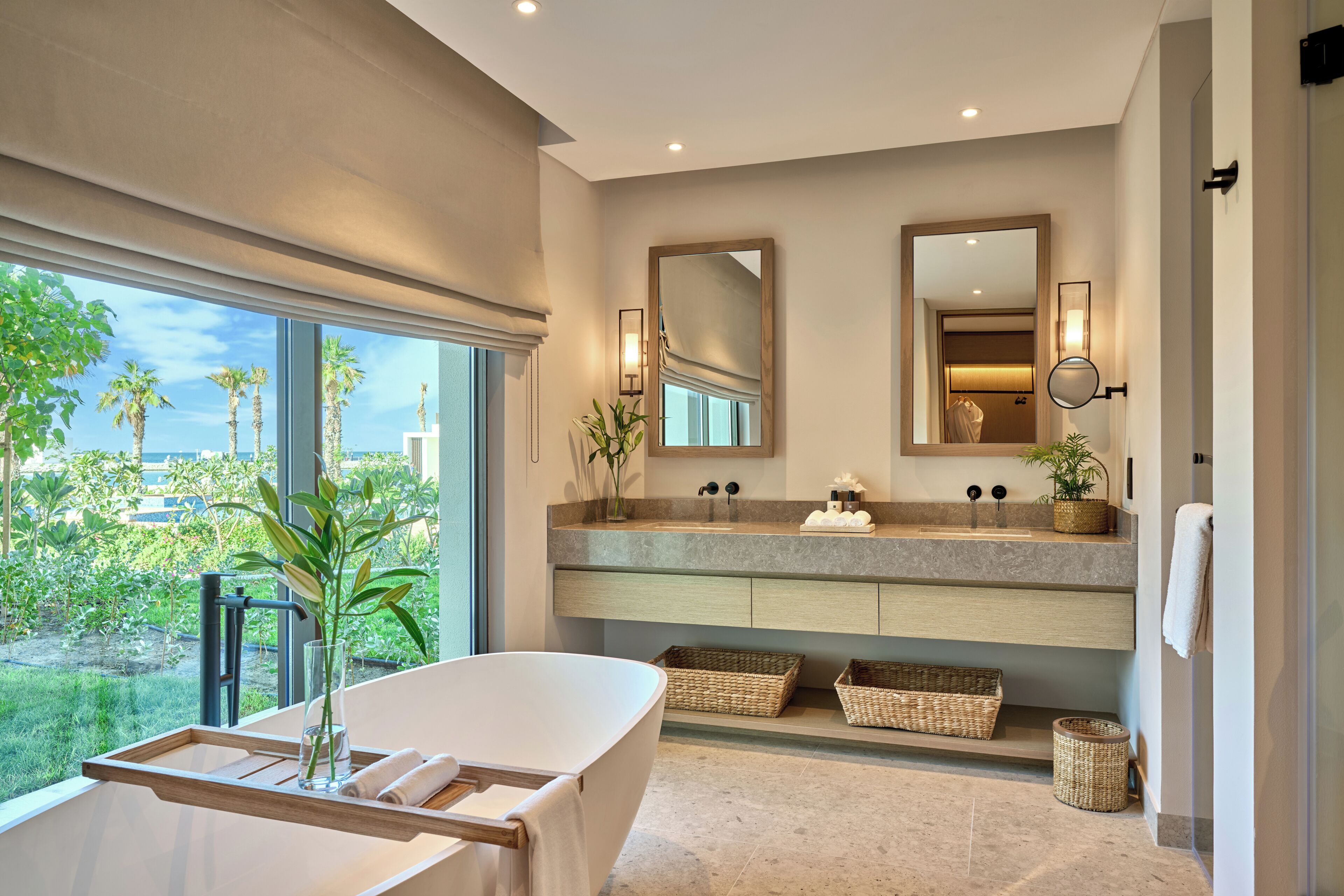 A modern bathroom with a large window, a bathtub, a vanity with a mirror, and a view of palm trees.