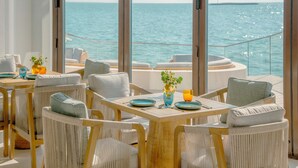 A dining area with wicker chairs and a wooden table, overlooking the sea. - Hawar Resort By Mantis (Hawar)