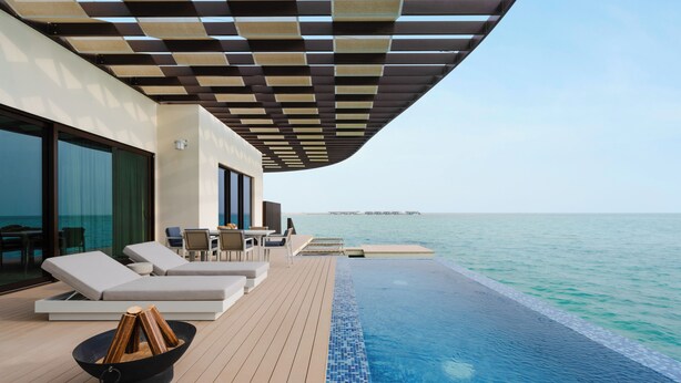A modern outdoor pool area with lounge chairs and a wooden fire pit, overlooking a calm sea. - Hawar Resort By Mantis (Hawar)