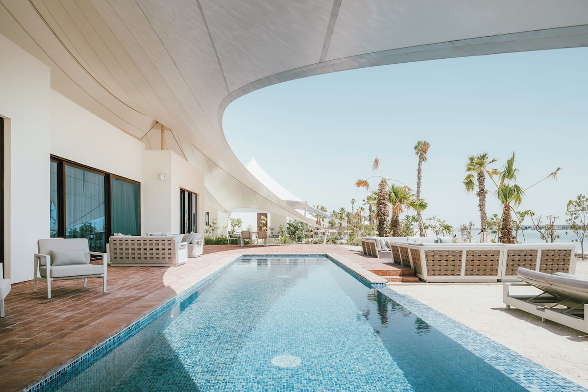 A modern infinity pool with a clear view of the ocean, surrounded by lounge chairs and a covered seating area.