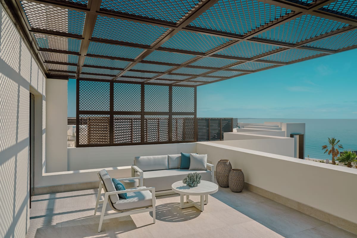 A modern outdoor seating area with a sofa, chairs, and a round table, overlooking a scenic view of the sea.