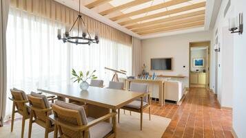 Un comedor amplio con una mesa y sillas de madera, una araña y vistas a la cocina al fondo.