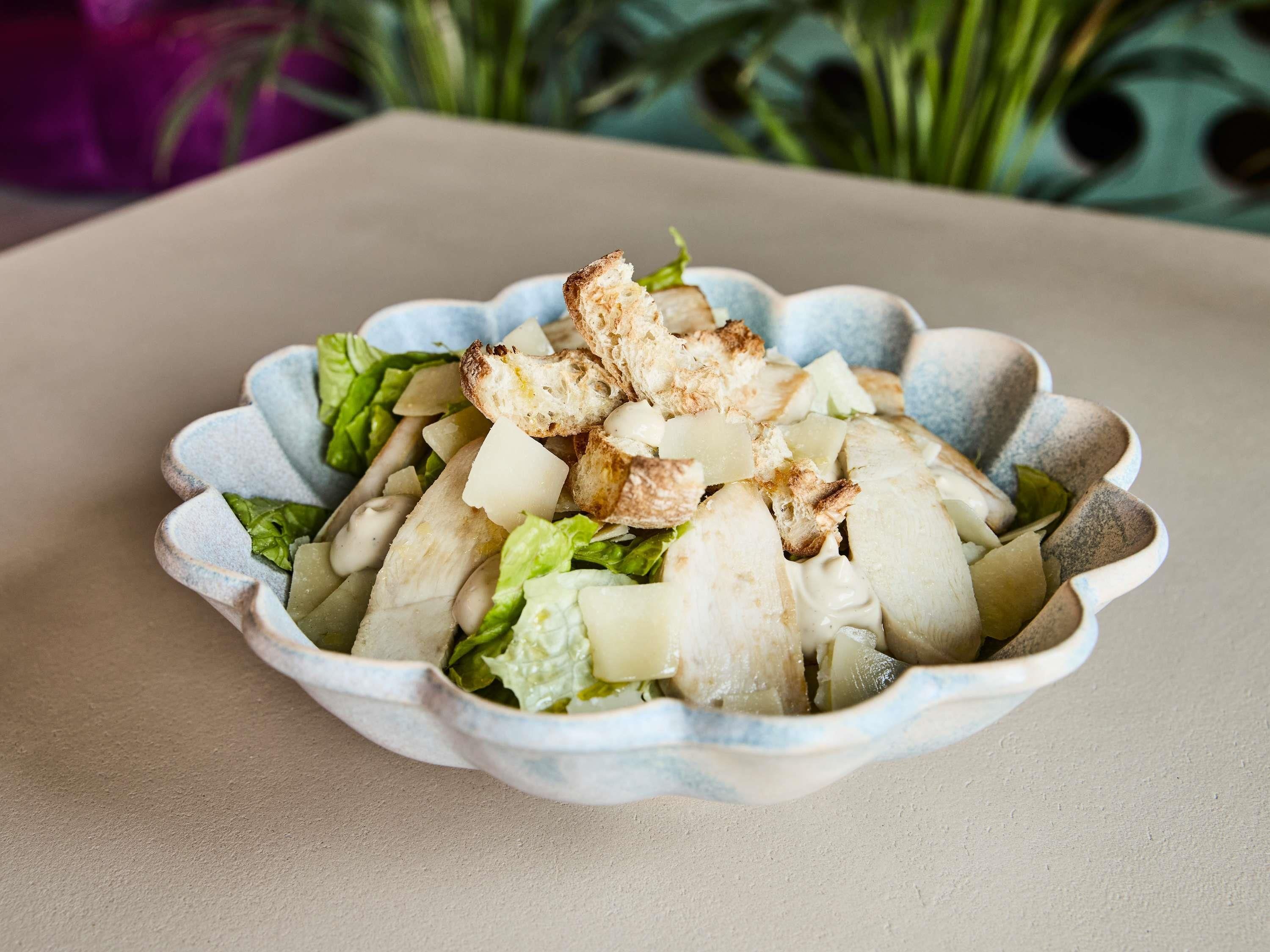 A bowl of salad with croutons and lettuce on a beige surface.