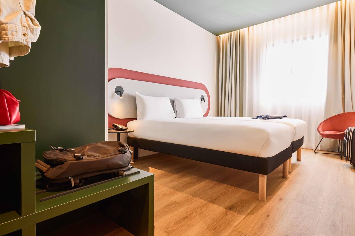 Une chambre d’hôtel avec un lit, une table de chevet, une lampe, une chaise et une valise.