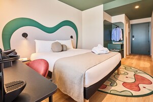 Siististi järjestetty hotellihuone, jossa on sänky, työpöytä ja tuoli.