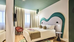 Ein modernes Hotelzimmer mit einem Bett, einem Sessel, einem kleinen Tisch und einem großen Fenster mit Vorhängen.