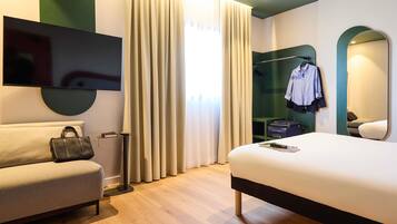 Habitació d'hotel moderna amb llit, sofà, televisió, mirall i armari.