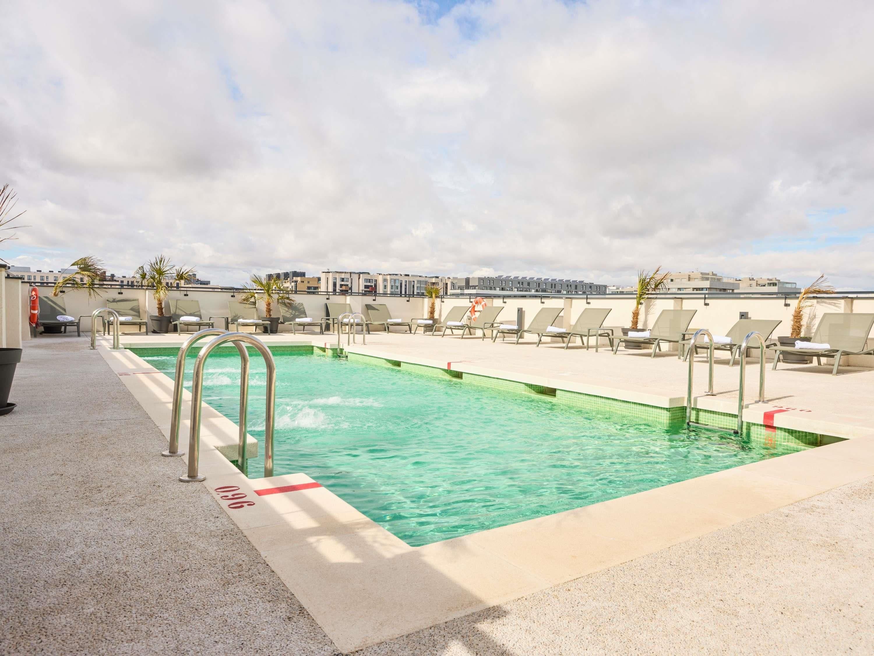 A rooftop pool with clear water, lounge chairs, and a view of buildings in the background.