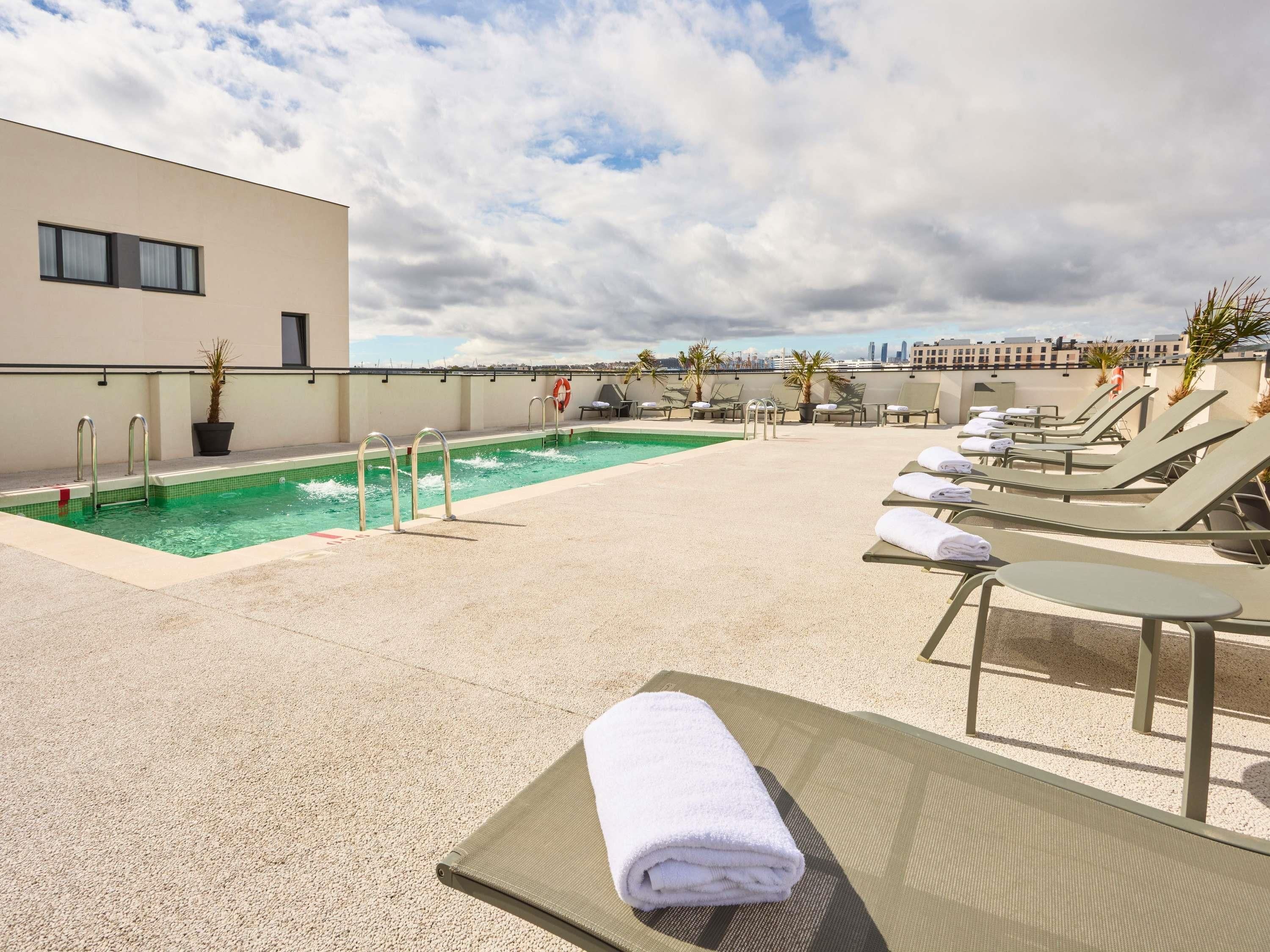 A rooftop pool with lounge chairs and a city view.