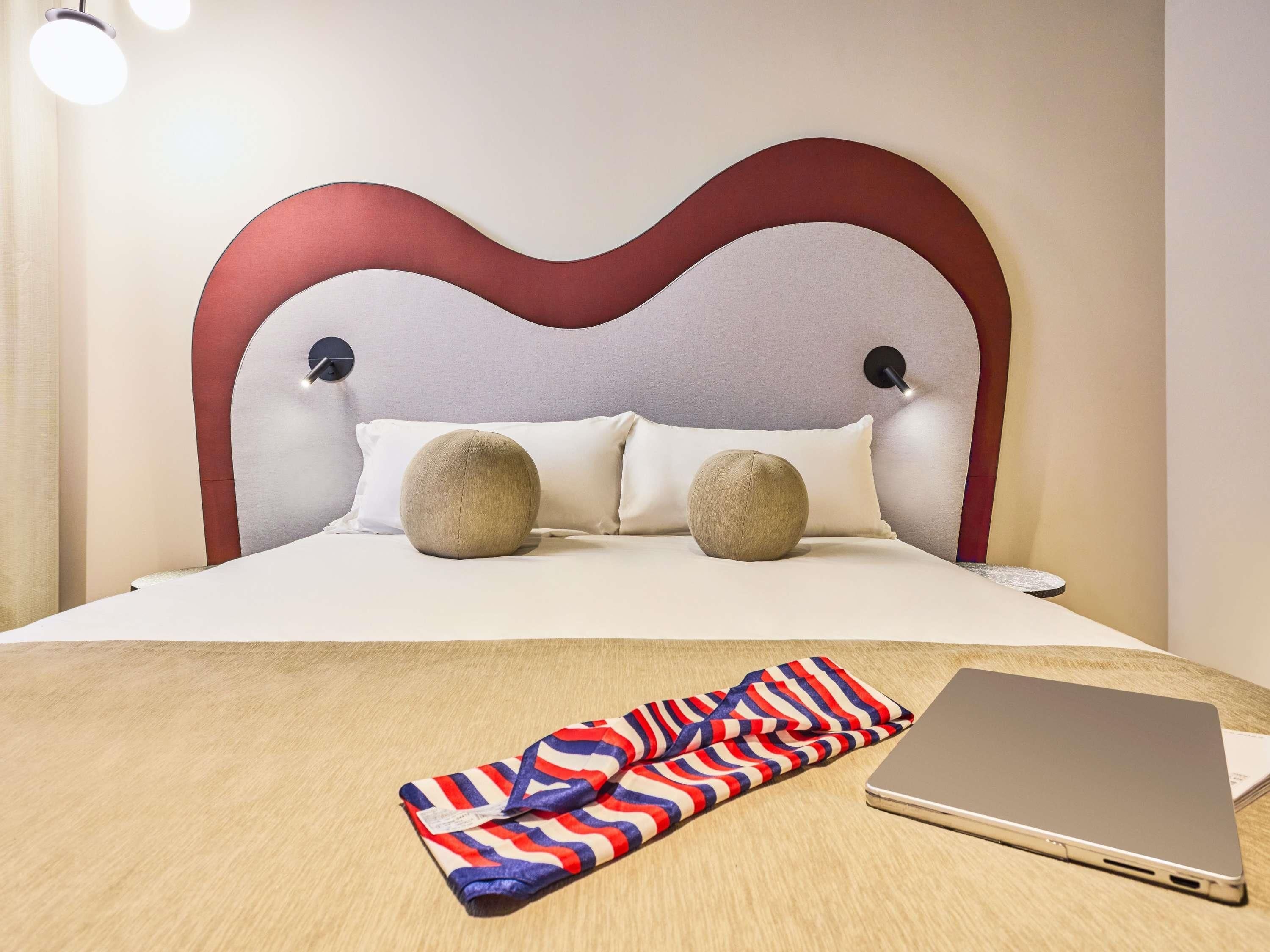 Ein Bett mit modernem Kopfteil, zwei Kissen, ein Laptop und ein gestreiftes Tuch auf einer Holzeinrichtung.