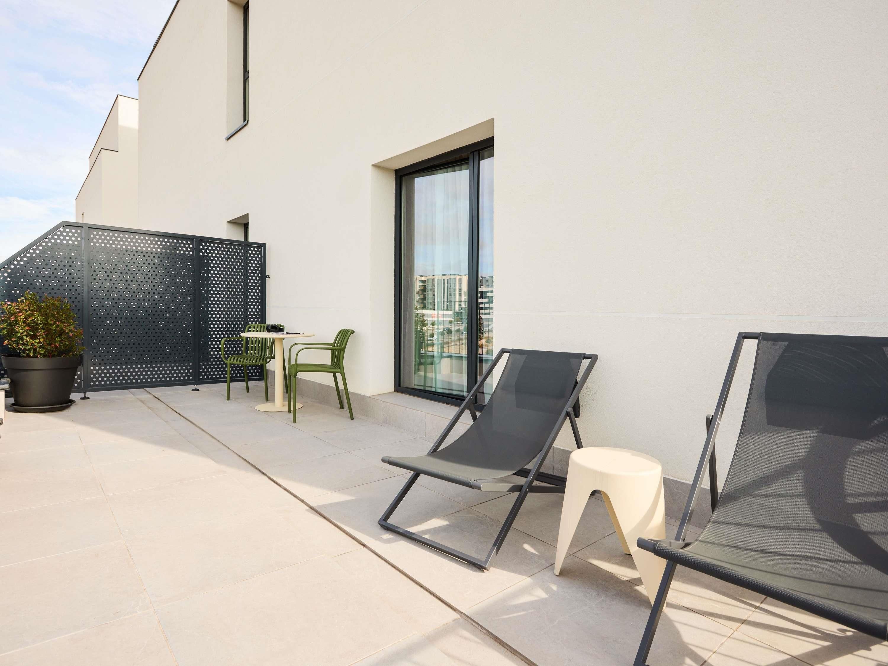 Een terras op het dak met een tafel en stoelen, twee loungestoelen, een potplant en een glazen deur die naar een balkon leidt.