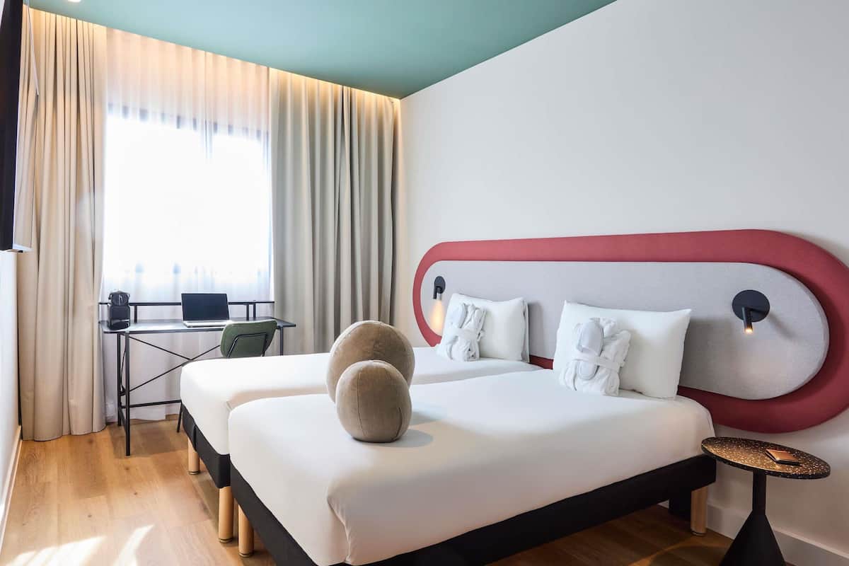 Une chambre d’hôtel avec un lit, un bureau, une chaise et une fenêtre avec des rideaux.