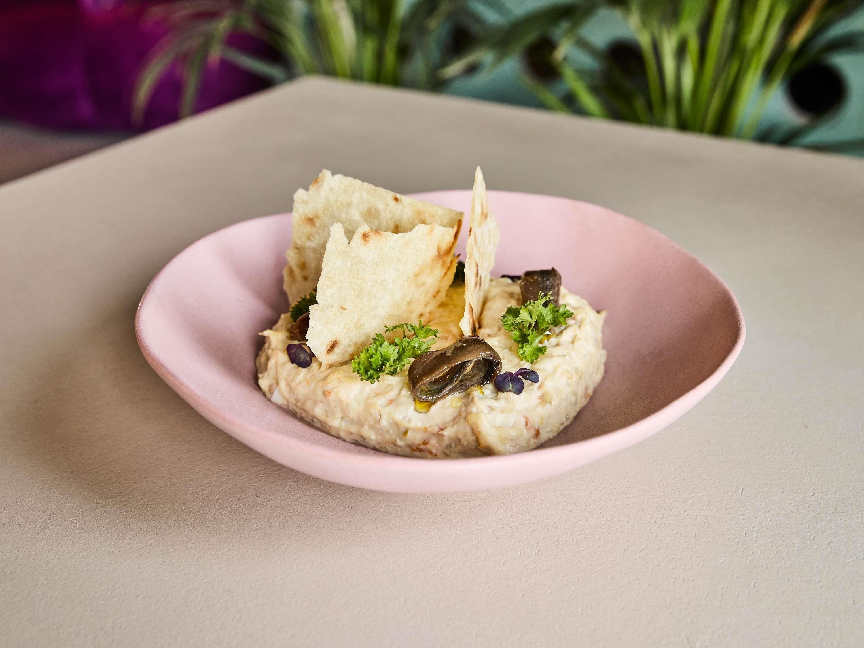 A pink plate with a food item, garnished with parsley and mushrooms, on a table.