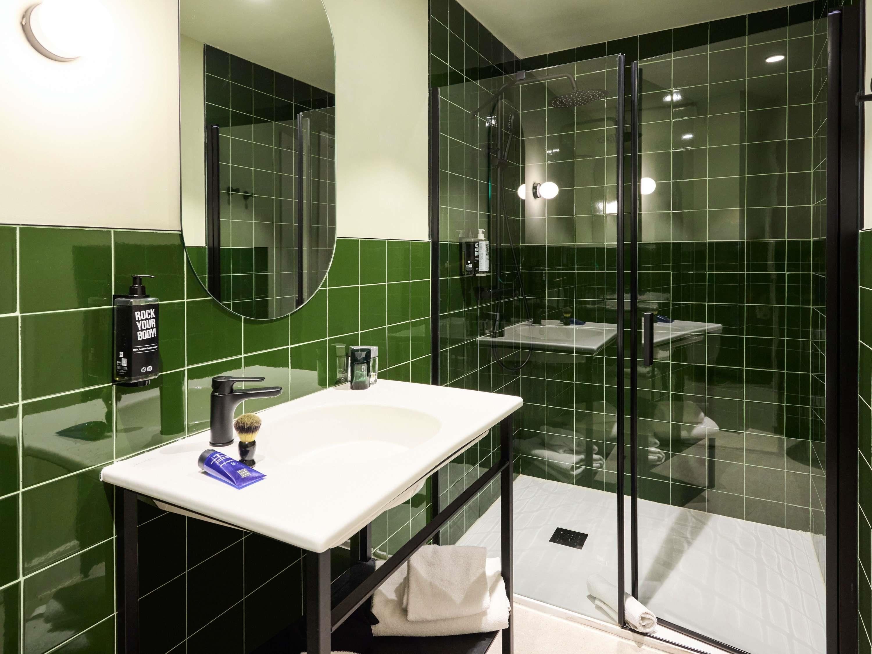 A bathroom with a white sink, a mirror, a glass-enclosed shower, and green tiles.