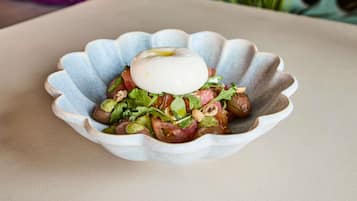 A scalloped bowl containing a salad with greens, tomatoes, and a poached egg on top.