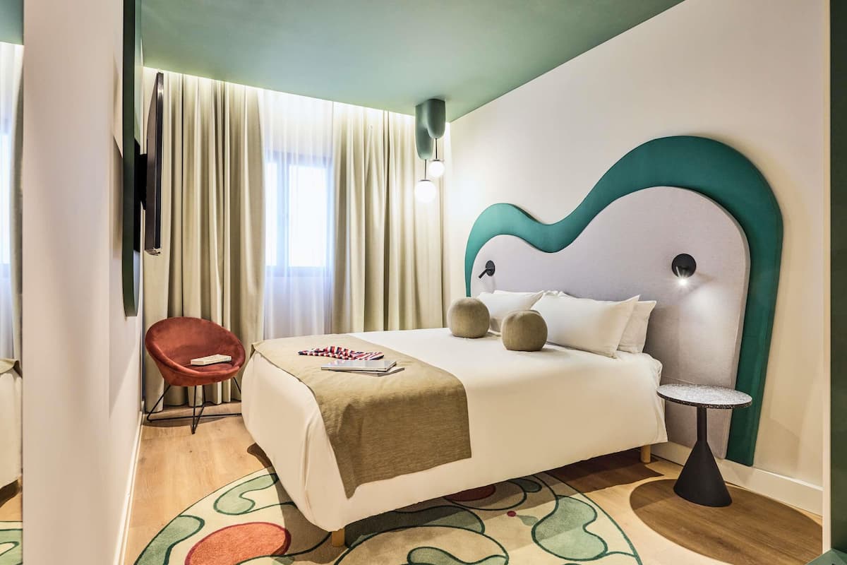Une chambre d’hôtel moderne, équipée d’un lit, d’une chaise, d’une petite table et d’une grande fenêtre avec des rideaux.