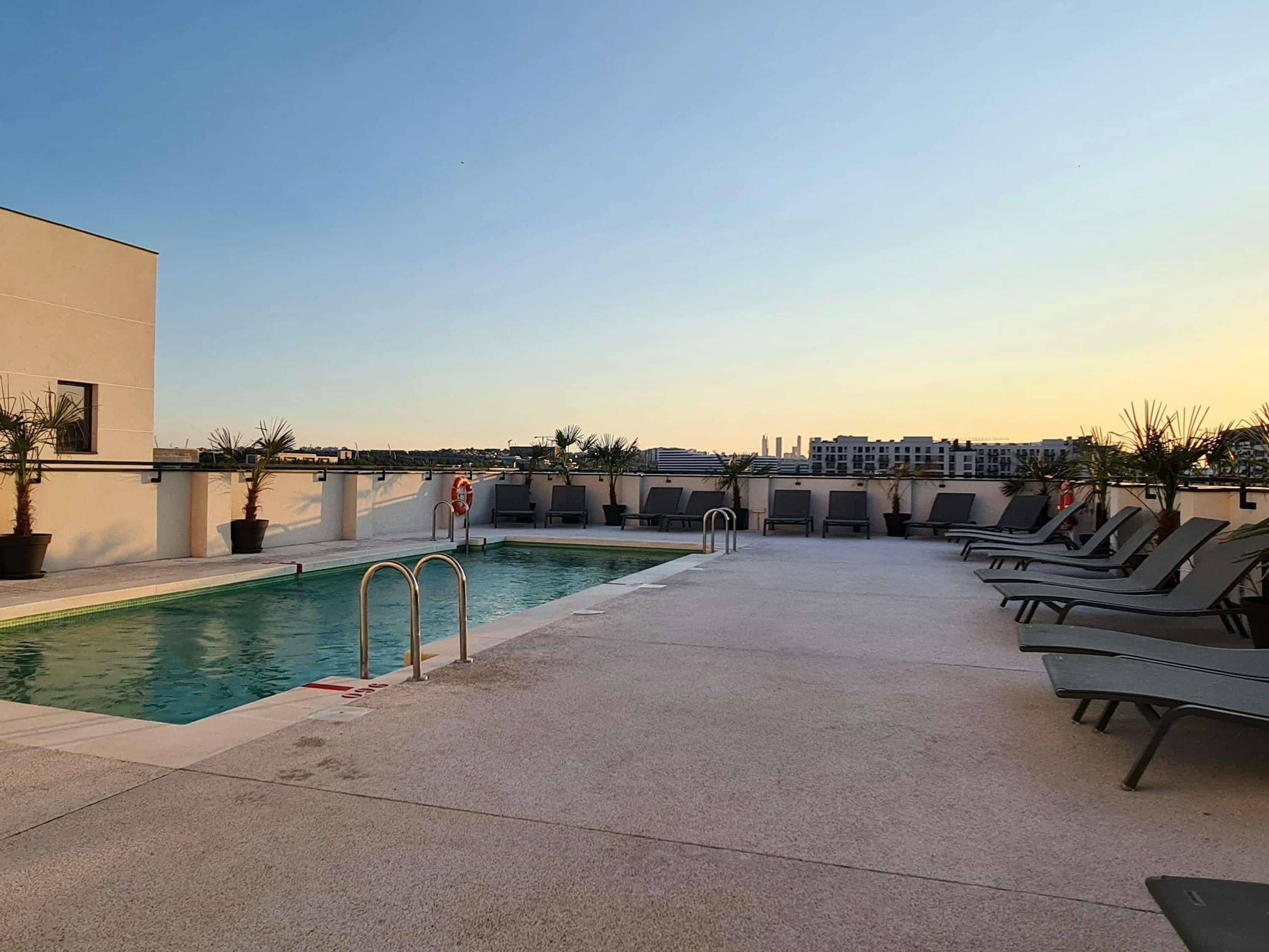 Área de piscina en la azotea con piscina, sillas de descanso y plantas en macetas.