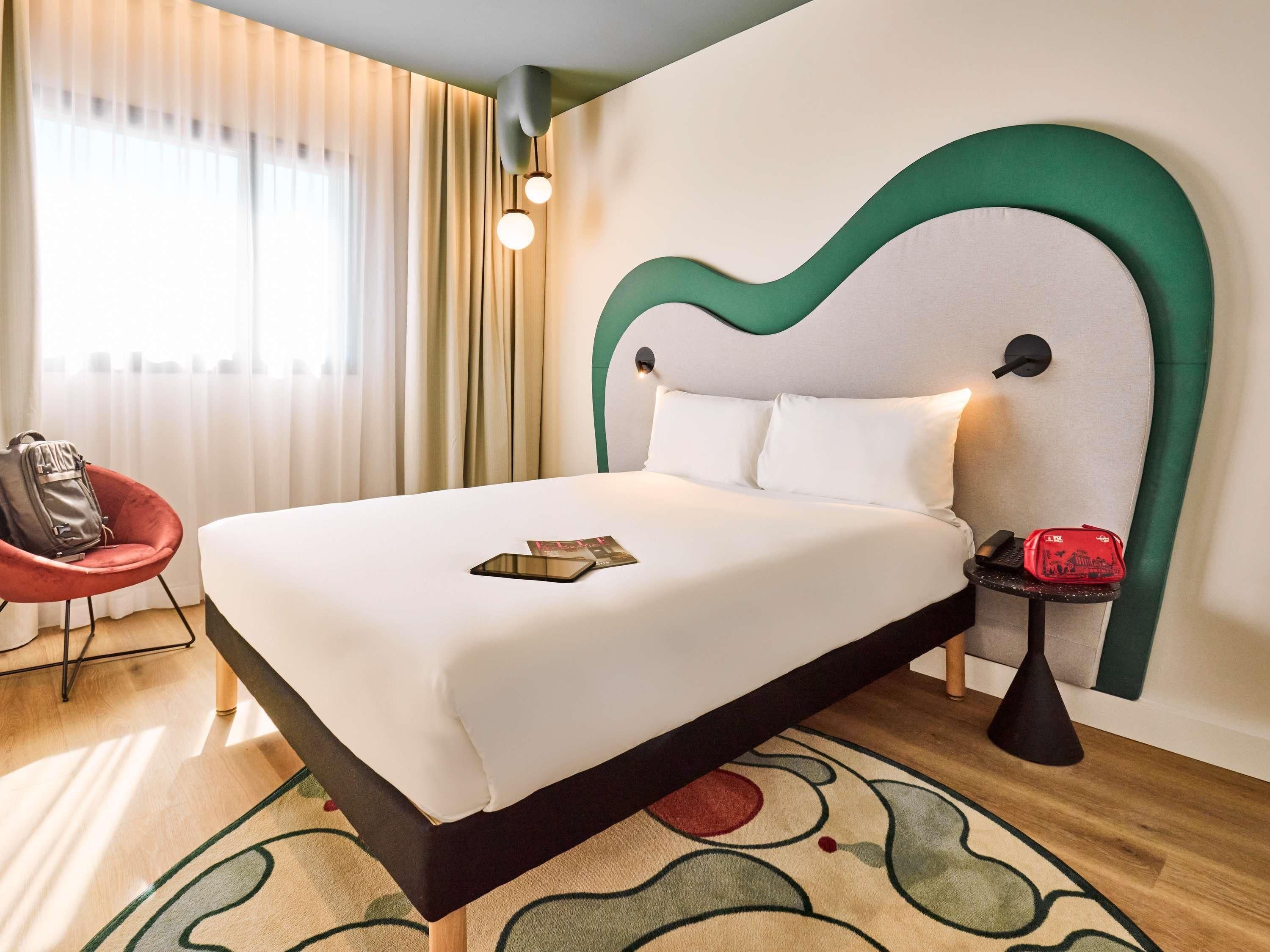 Una habitación de hotel con cama, una silla, una mesita y una lámpara.