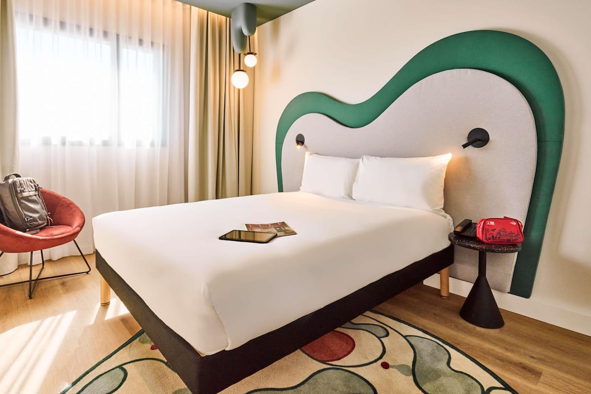 Une chambre d’hôtel avec un lit, une chaise, une petite table et une lampe.