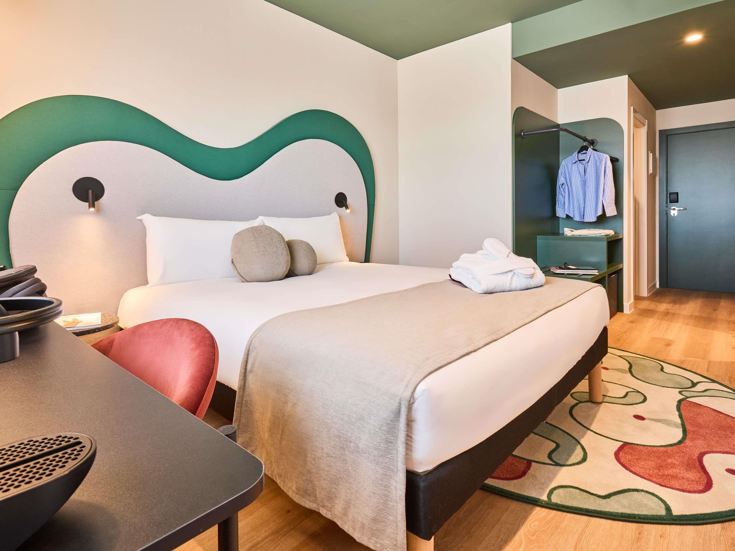 A hotel room with a bed, bedside table, chair, and a bathroom visible through an open door.