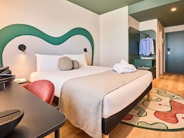 Ein Hotelzimmer mit Bett, Nachttisch, Stuhl und einem durch eine offene Tür einsehbaren Badezimmer.