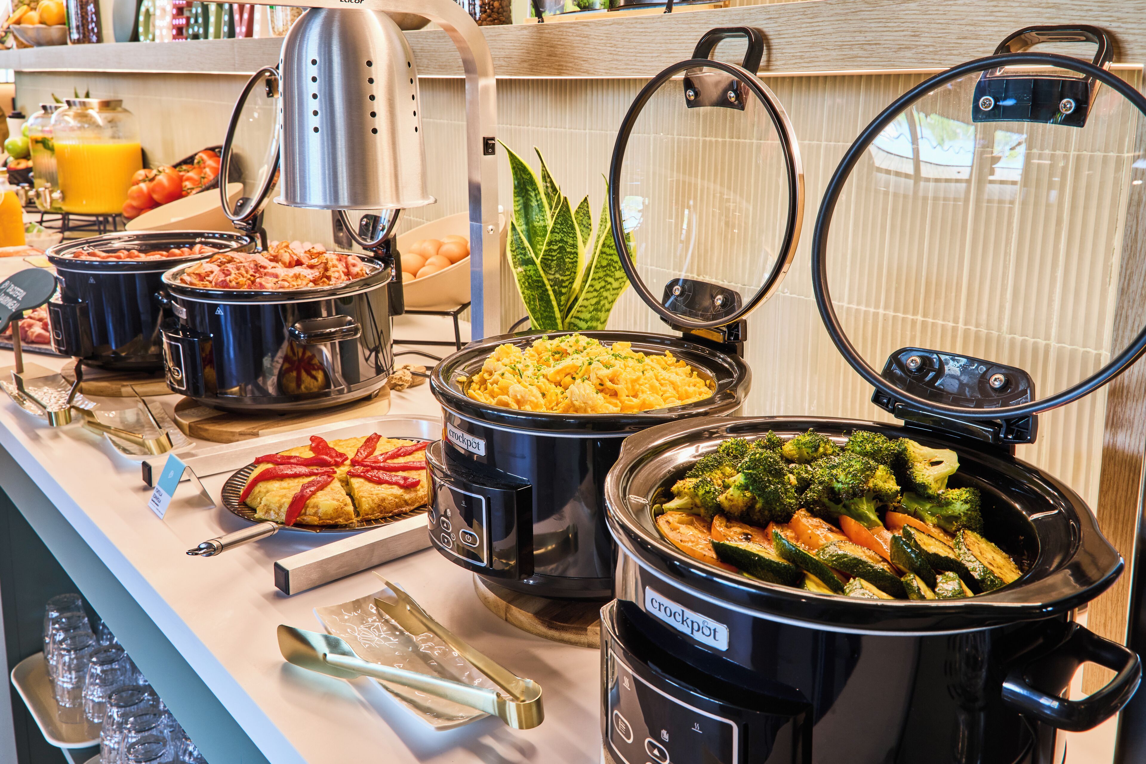 Een buffet met diverse gerechten in slowcookers, waaronder ovenschotels en groenten.