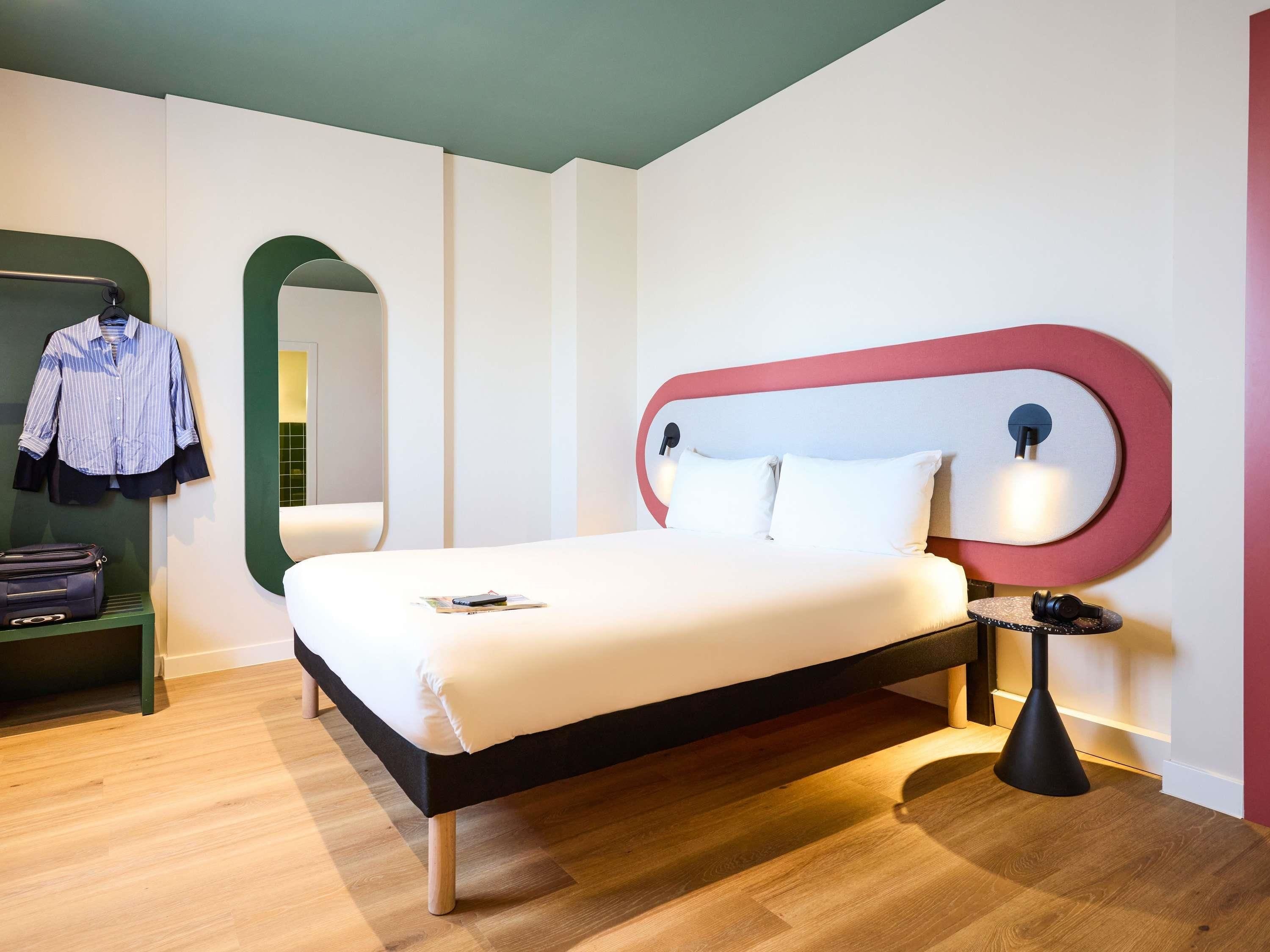 Una habitación de hotel moderna con una cama, una mesita de noche, una lámpara, un espejo y un armario.