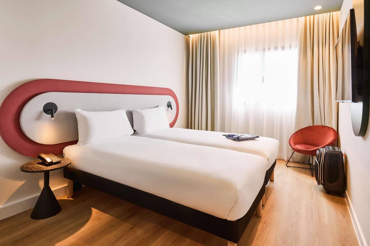 Une chambre d’hôtel avec un lit, une chaise, une valise et un téléviseur.