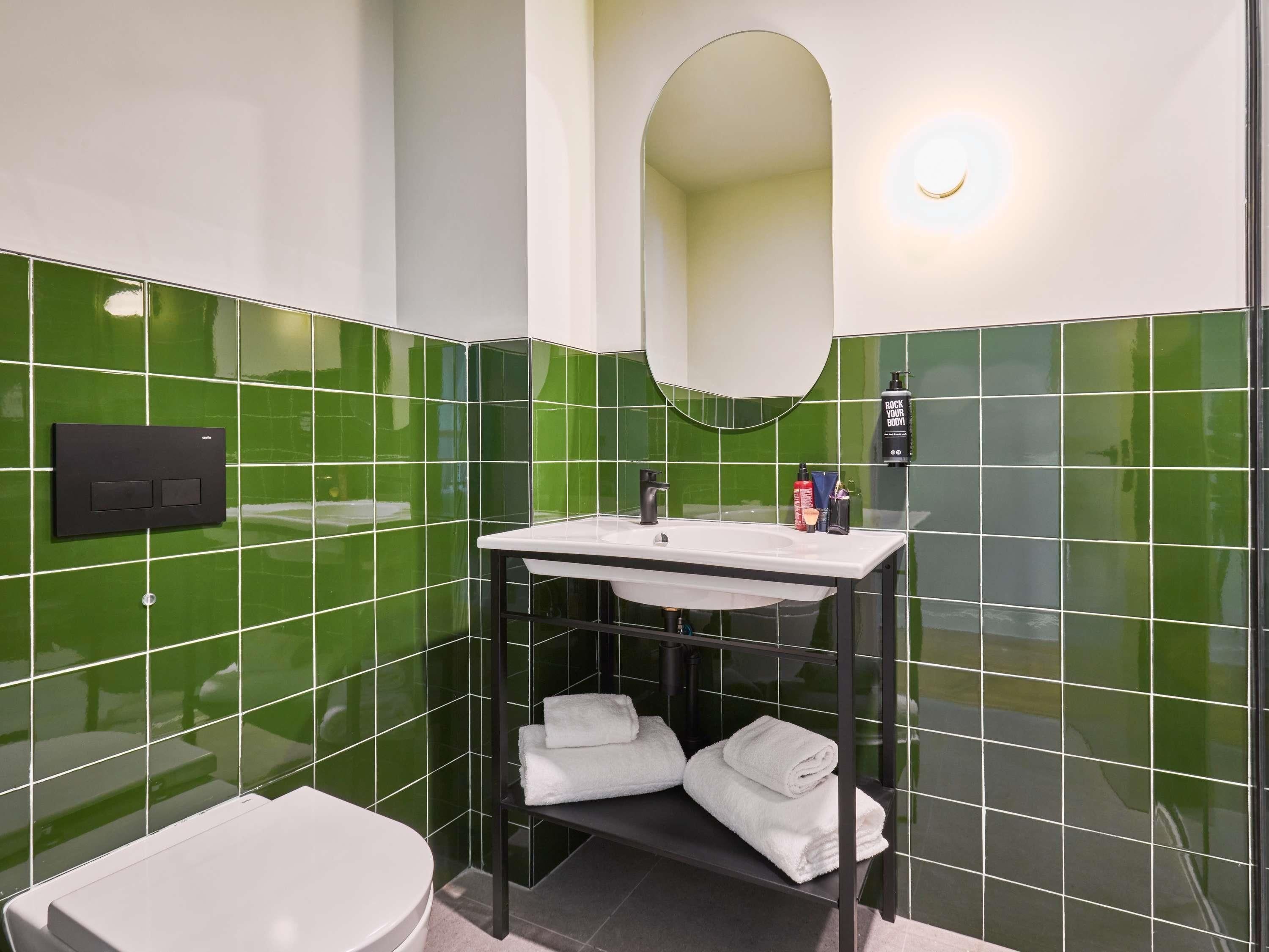 Ein Badezimmer mit grünen Fliesen, einem weißen Waschbecken, einem schwarzen Ablagefach mit Handtüchern und einer Toilette.