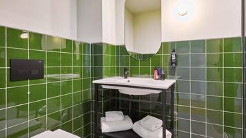 Ein Badezimmer mit grünen Fliesen, einem weißen Waschbecken, einem schwarzen Ablagefach mit Handtüchern und einer Toilette.
