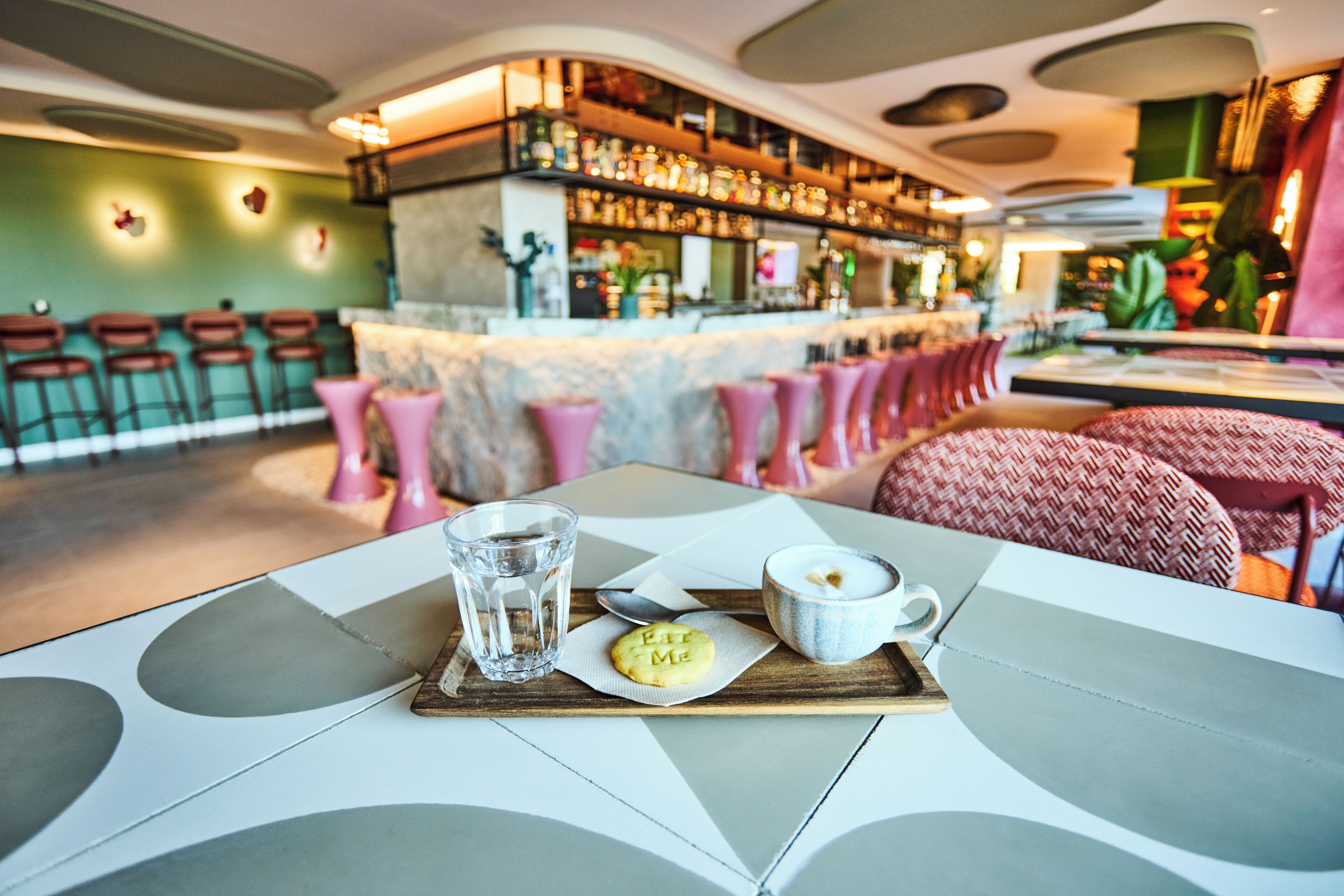 A bar area with stools, a bar counter with bottles, and a table with a tray of food and drinks.
