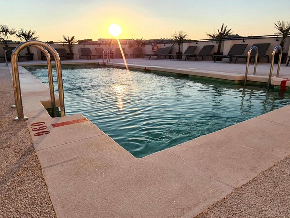 Ein Pool mit sonnendurchflossenem Wasser, Liegestühlen und einem Rettungsring.