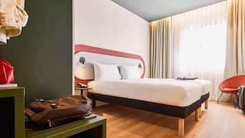 Une chambre d’hôtel avec un lit, une table de chevet, une lampe, une chaise et une valise.