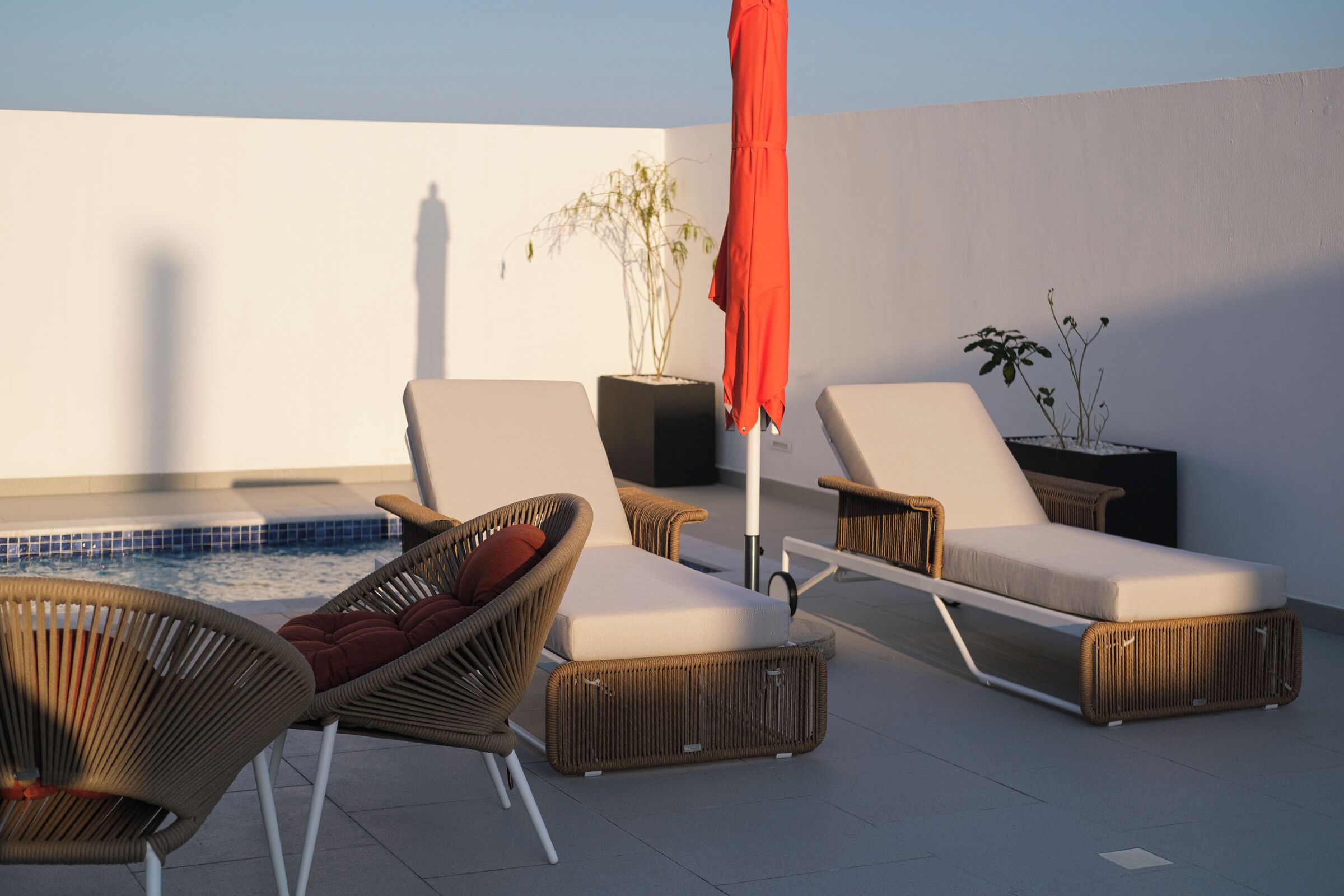 Un área de descanso en la azotea con sillones de mimbre, una piscina pequeña y plantas en macetas.