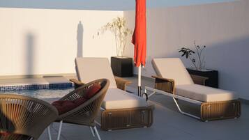 Un área de descanso en la azotea con sillones de mimbre, una piscina pequeña y plantas en macetas.