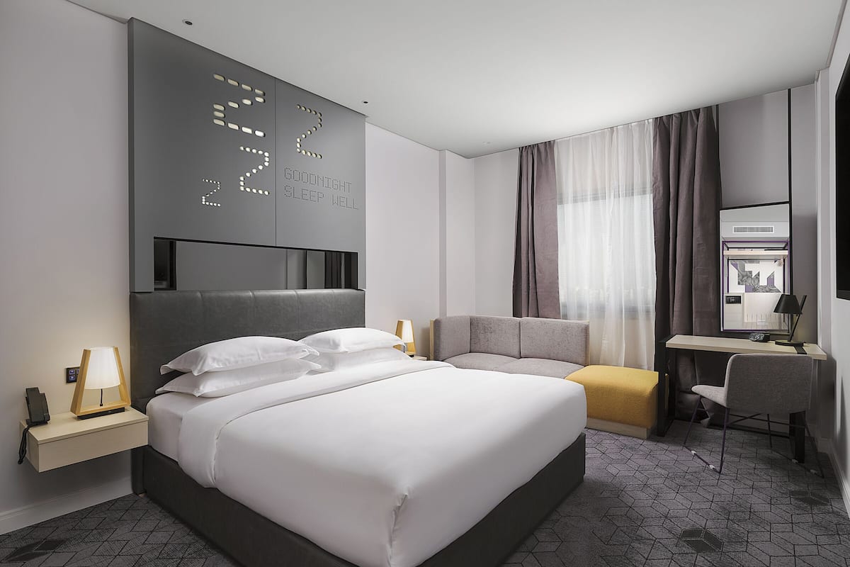 A modern hotel room with a large bed, bedside tables, a desk, and a comfortable seating area.