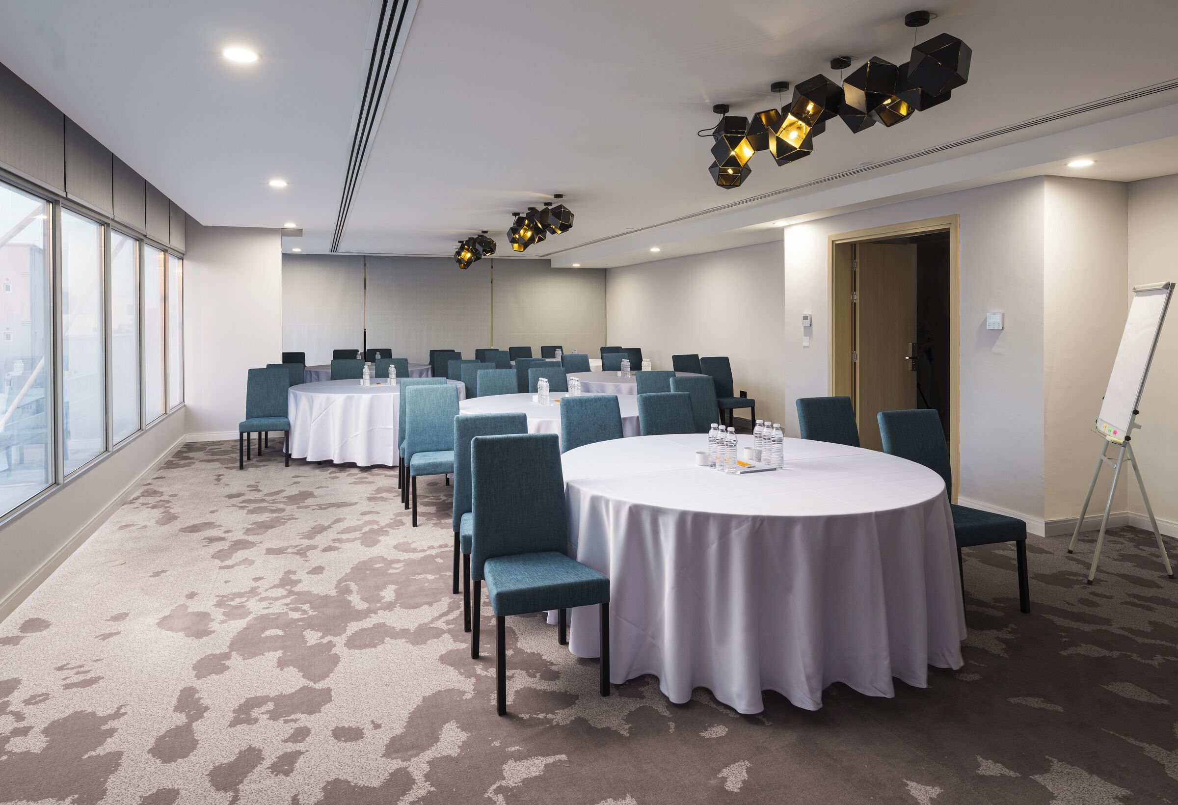 Un salón de conferencias con mesas redondas, sillas color turquesa y piso alfombrado.