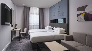 A modern hotel room with a bed, two bedside tables, a sofa, a TV, and a city view.