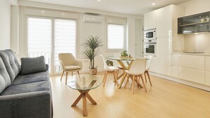 A modern living room with a grey sofa, a glass coffee table, and a dining area with white chairs and a glass table.