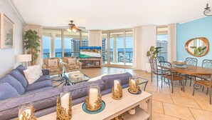 Un salon spacieux avec un grand canapé, une table à manger avec des chaises et un balcon offrant une vue sur la ville et la mer.