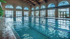 Une piscine intérieure à l’eau claire, entourée de grandes baies vitrées qui offrent une vue sur les palmiers et la mer.