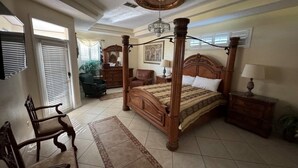 Une chambre spacieuse avec un lit à baldaquin, une chaise en bois, une table de chevet et un lustre.