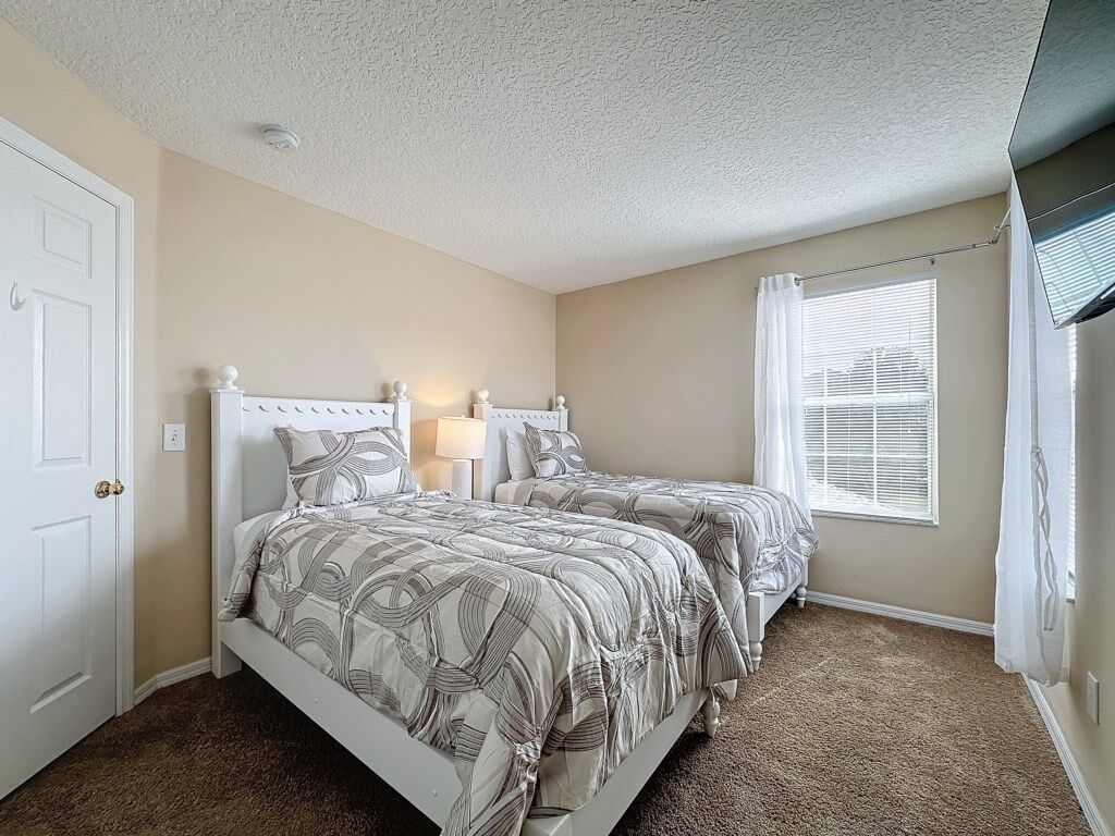 A bedroom with two beds, a window with blinds, and a door.