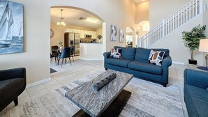 Ein geräumiges Wohnzimmer mit einem blauen Sofa, einem Couchtisch und einer Treppe, die in eine obere Ebene führt.
